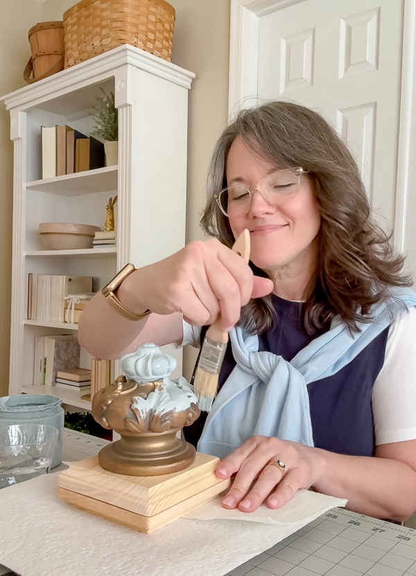 Linda McDonald of Life on Summerhill painting a vintage wood finial on a square wood base with Dixie Belle Savannah Mist chalk paint to make a DIY patriotic finial flag stand