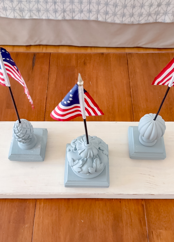 Three DIY patriotic finial flag stands painted in Dixie Belle Savannah Mist chalk paint with small Betsy Ross stick flags grouped together in odd numbers for a 4th of July centerpiece display