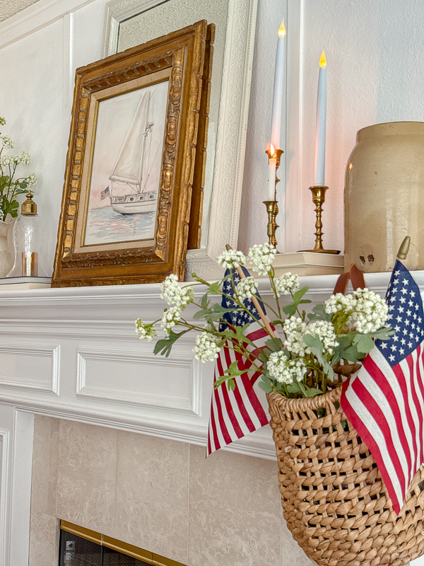 Woven wall basket with American flags and white flowers hanging on a fireplace pillar for coastal Americana decor