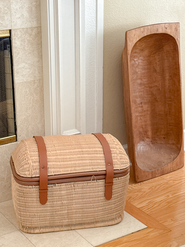 Vintage wicker trunk with leather straps and a wooden dough bowl styled on a hearth for year-round Americana decor