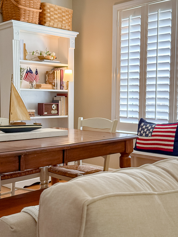 Ralph Lauren Americana living room with vintage wooden sailboat model on a farm table, white bookcase with flags, and slipcovered sofa