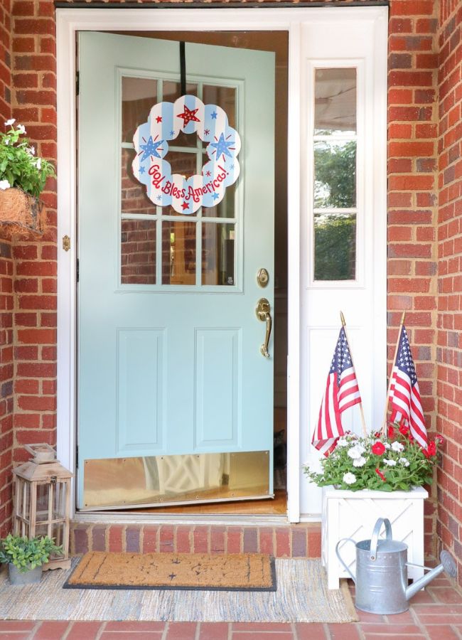 Simple patriotic porch decor with a Coton Colors wreath, stick flags, and red and white flowers