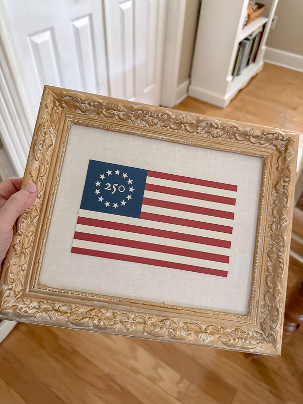 250th Betsy Ross American flag framed on fabric inside a ornate gold frame.