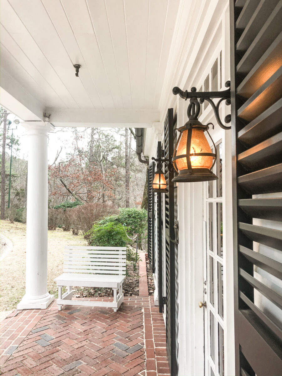 Black and metal and glass globe wall sconce on the exterior of a home at Roosevelts home. The exterior is white shiplap with black louver shutters. Fantastic idea for a new build.