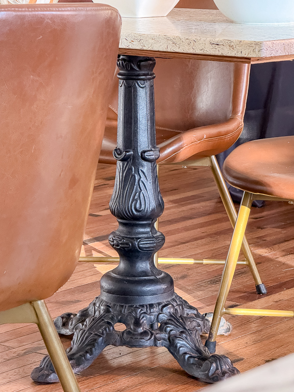 Ornate cast iron table base paired with modern leather and brass chairs