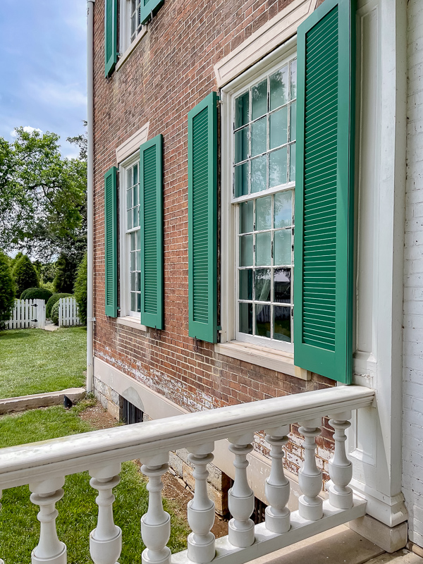 Exterior of the Hermitage with brick and bright green shutters. Notice the 12 over 16 windows. These are very old windows. Also trim on top of window. Details to consider for newer build homes.