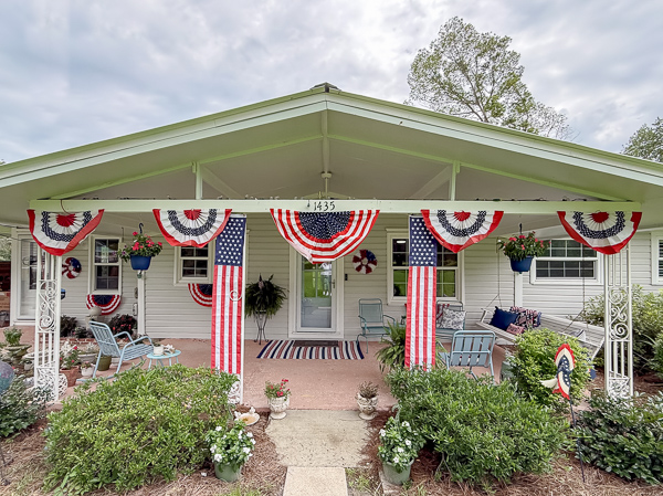 Large patriotic porch decor with a swing, flag pillows, and swags across the front