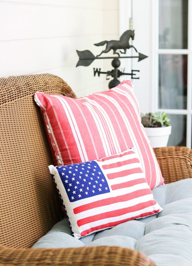 Red and white striped pillow and American flag pillow on a wicker porch chair