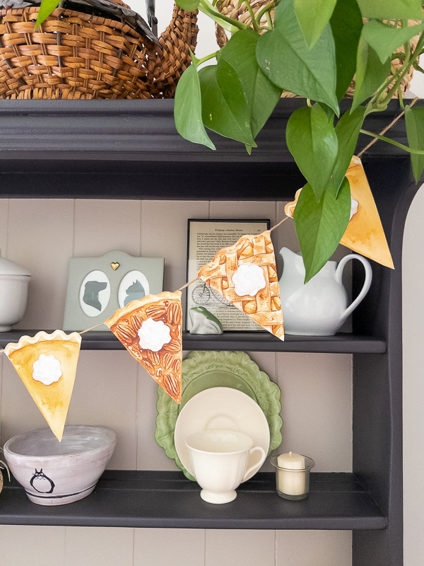 Thanksgiving pie garland printable with watercolor pie slices strung on a dark hutch shelf