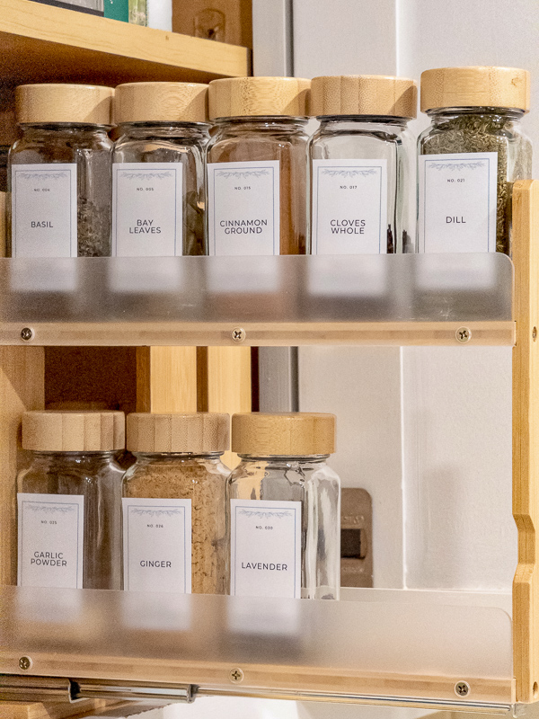Glass spice jars with vintage numbered labels for basil, bay leaves, cinnamon, cloves, dill, garlic powder, ginger, and lavender organized in a pull-out cabinet drawer