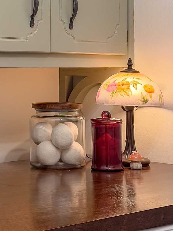 Vintage lamp, amber jar, glass jar with wool balls on a butcher block countertop in a cozy cottage laundry room