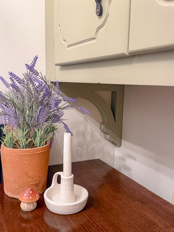 Lowe's faux lavender plant in terracotta pot, white candle and mushroom with a green bracket holding up cabinet