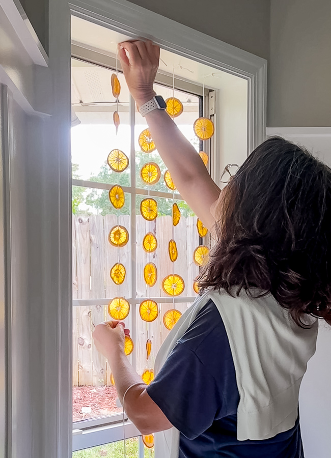 Taping dried orange suncatcher strands to the top of a window frame