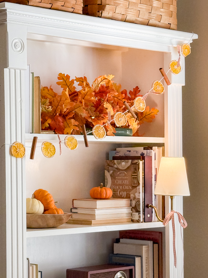 DIY dried orange garland with cinnamon sticks and gingham ribbon on a white bookcase styled for fall