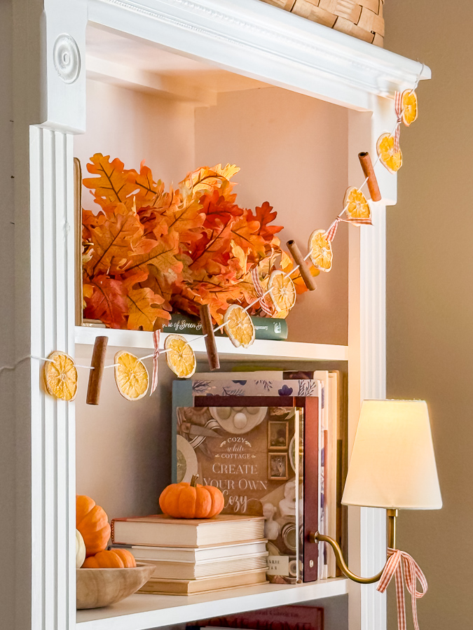 Dried orange garland swagged across bookcase shelves with a fall leaf garland and tiny pumpkins