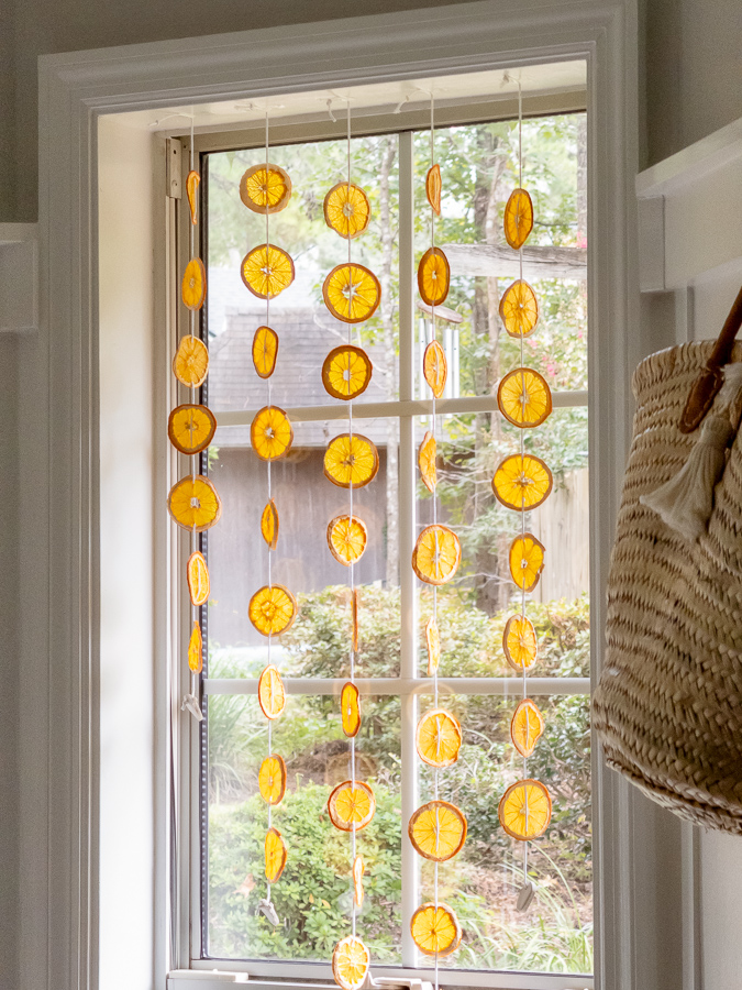 Five strands of dried orange slices hanging in a window as a fall suncatcher