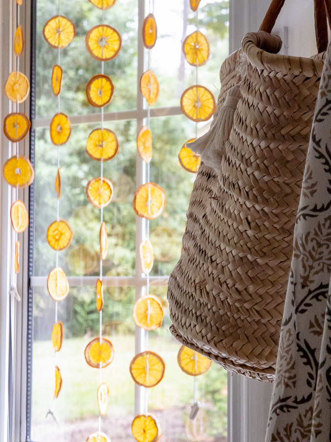 Dried orange suncatcher in a window beside a woven straw tote
