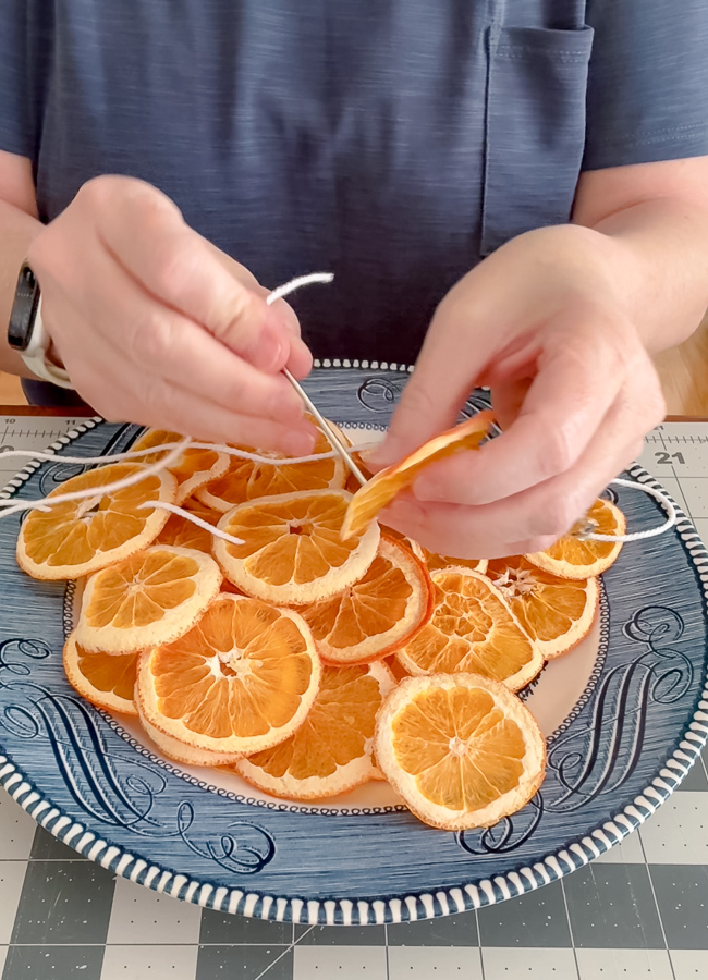 Threading a needle and twine through a dried orange slice for a suncatcher
