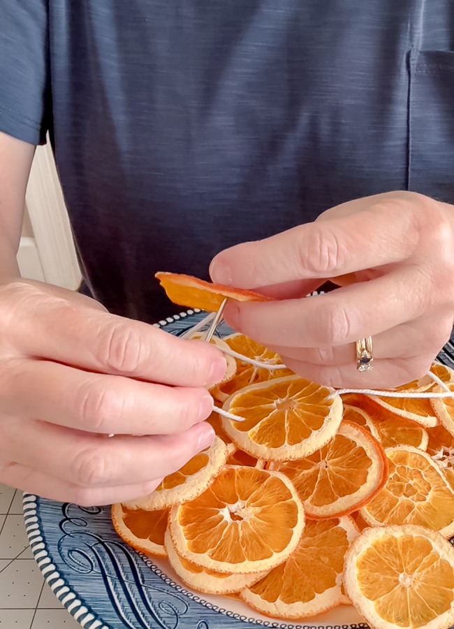 Close-up of hands pushing a yarn needle through a dried orange slice