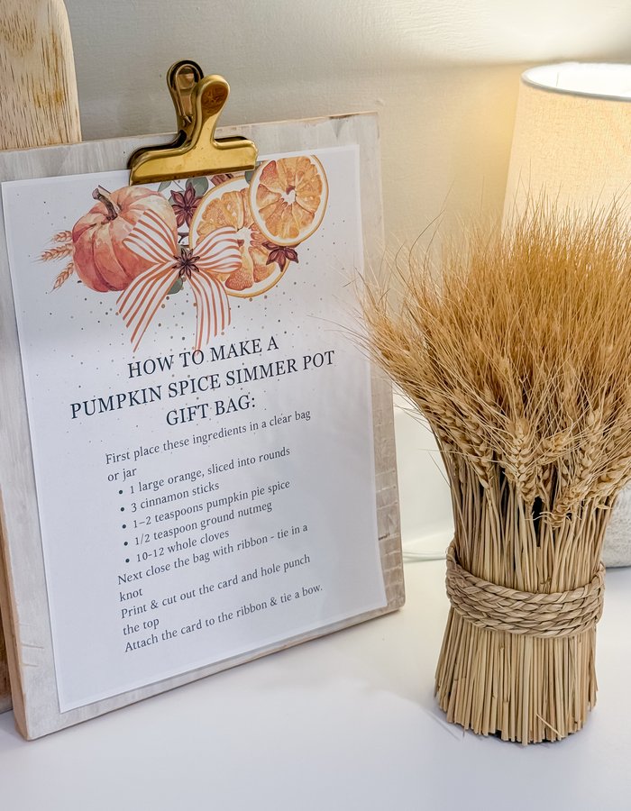 Pumpkin spice simmer pot recipe card on a clipboard next to a bundle of dried wheat and a lit kitchen lamp