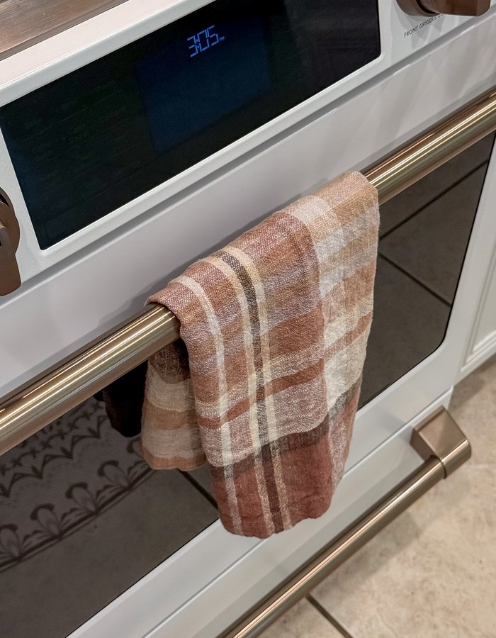Close-up of a plaid dinner napkin repurposed as a dish towel, hanging on the oven door handle