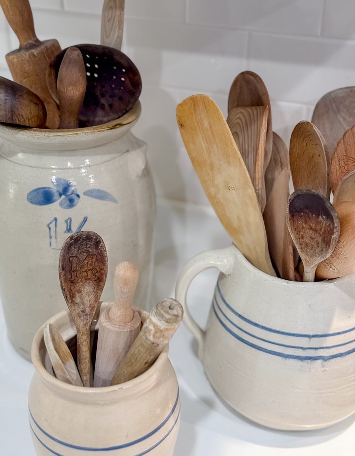Close-up of wooden spoons, a wooden reamer, and a vintage perforated spoon collected in salt-glazed crocks and pitchers