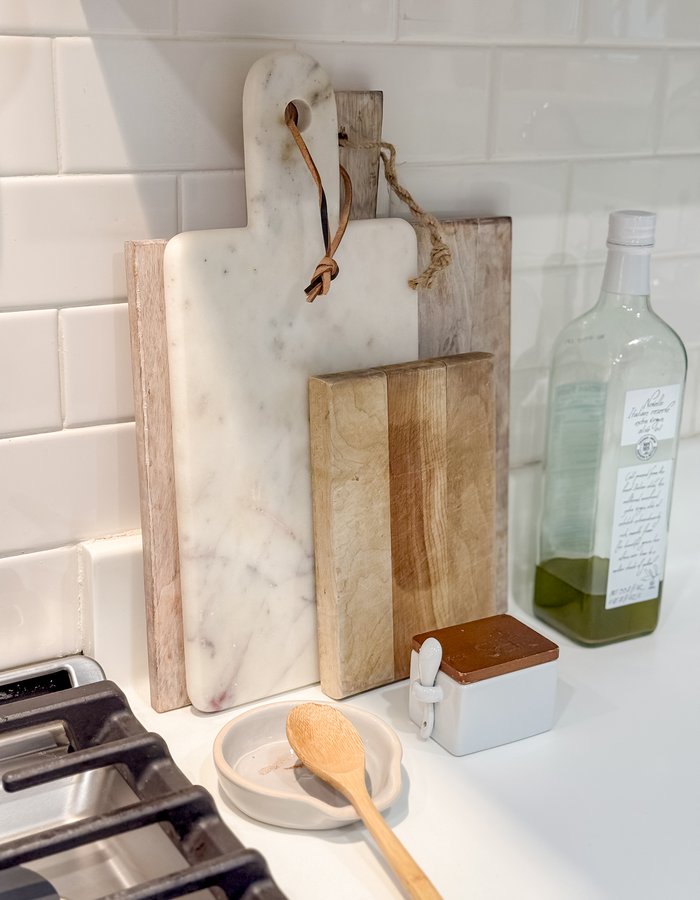 Marble and wood cutting boards leaning on the counter next to olive oil and a small butter crock