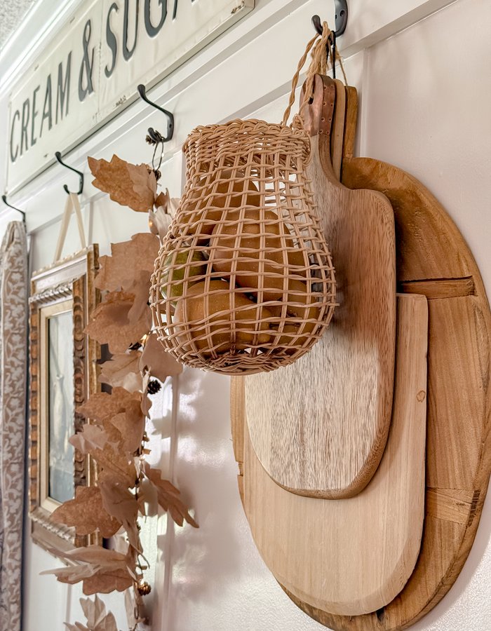 Woven garlic basket filled with faux yellow and green pears, hanging next to wooden cutting boards