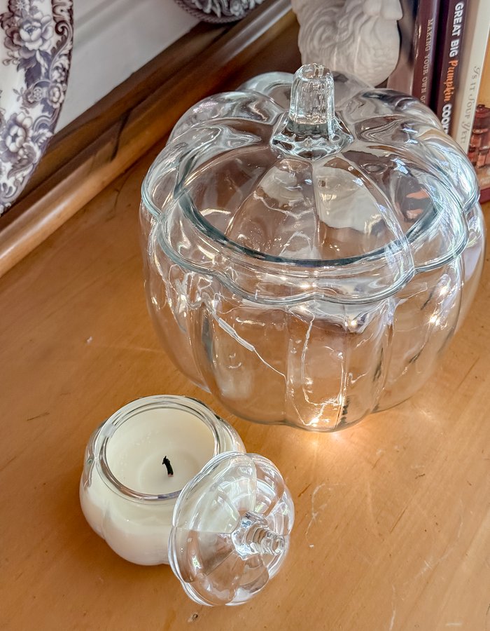 Glass pumpkin-shaped cookie jar and a small glass candle beside a stack of cookbooks