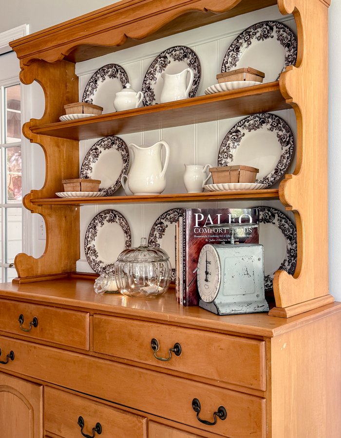 Wooden hutch styled for fall with brown and white Spode dishes, white ironstone pitchers, berry baskets, and a vintage kitchen scale