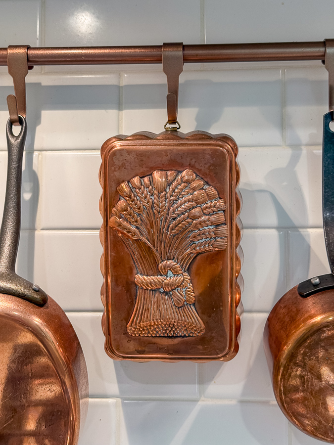 Copper mold with wheat design hanging on a tile wall for a kitchen fall french country design