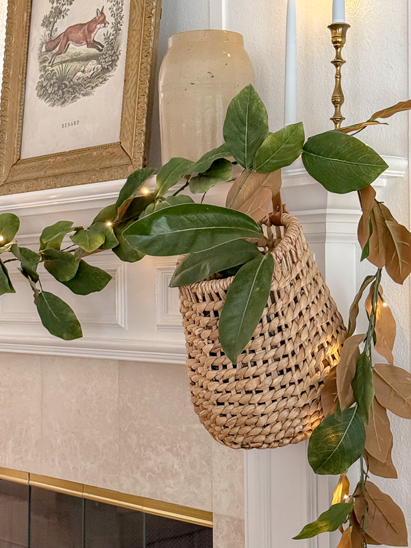 Magnolia garland trailing into a hanging woven basket strung with fairy lights on the mantel