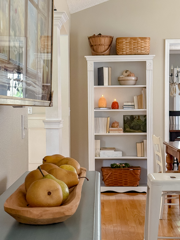 Wood dough bowl filled with pears on the kitchen counter, with a styled bookcase in the background