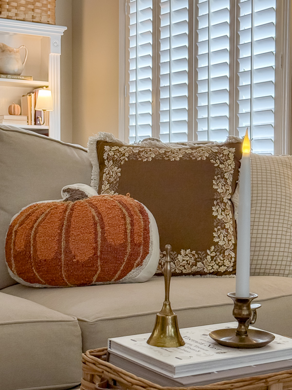 Needlepoint pumpkin pillow layered with an embroidered acorn pillow on the couch, next to a brass candlestick