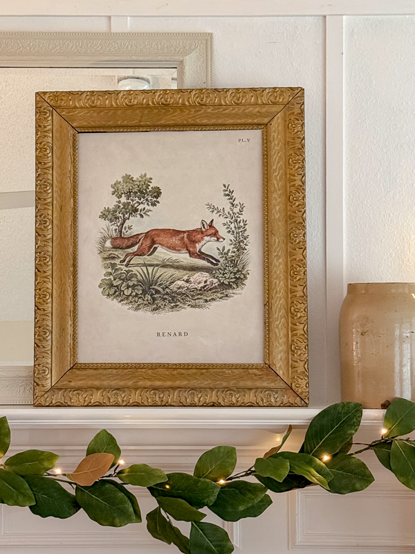 Fox print leaning on the mantel with an antique crock and magnolia garland strung with fairy lights