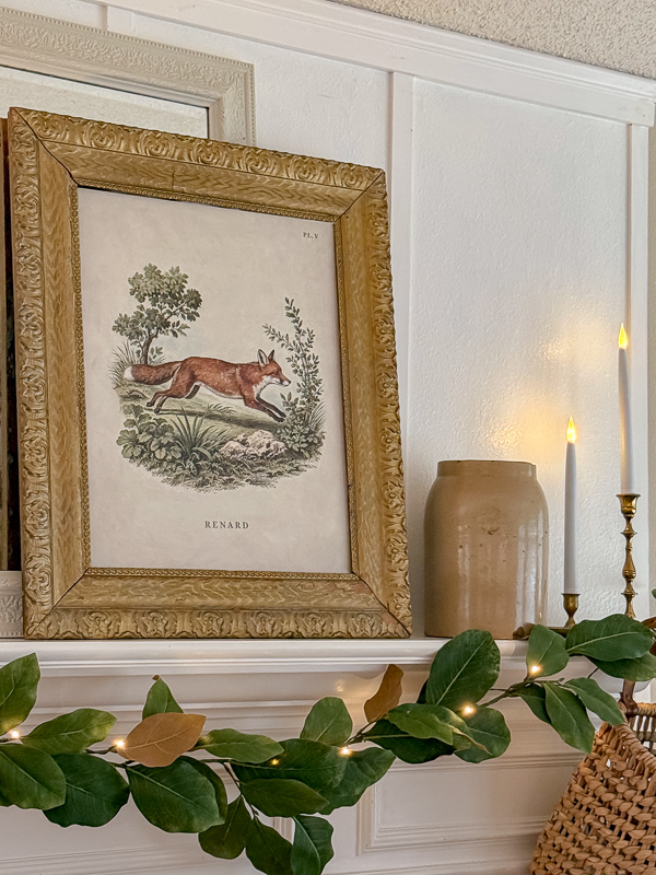 Fox print art next to an antique crock and brass candlesticks on the mantel, shopped from around the house