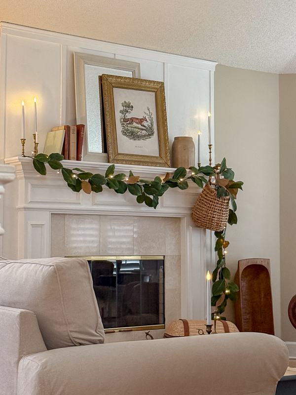 Living room view of the green and brown fall mantel with magnolia garland and vintage art beside the slipcovered sofa