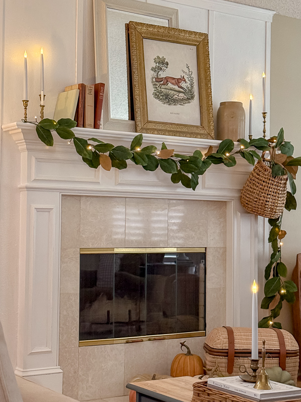 Heritage-inspired fall mantel with magnolia garland, a vintage fox print, brass candlesticks, and a hanging basket