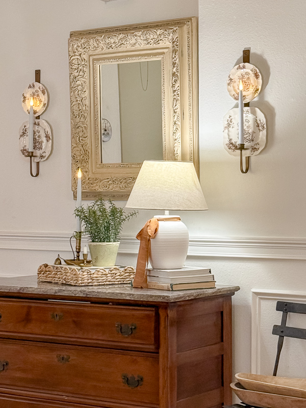 Close-up of a fall entryway dresser with floral porcelain candle sconces, a taper candle, and a small potted plant