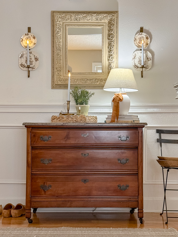 Fall entryway dresser vignette with a gilt mirror, wall candle sconces, and a lamp for a heritage-inspired look