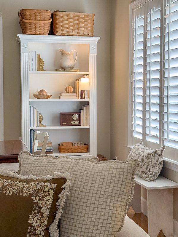 Entryway bench styled with plaid and ruffled fall pillows, with baskets and a pitcher on the shelf above