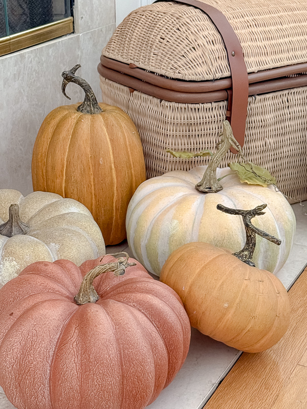 Best faux pumpkins by Pottery Barn styled on a fireplace hearth next to a wicker basket trunk