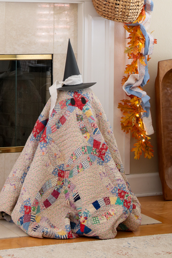 Vintage Double Wedding Ring quilt ghost wearing a black paper witch hat beside a lighted fall garland