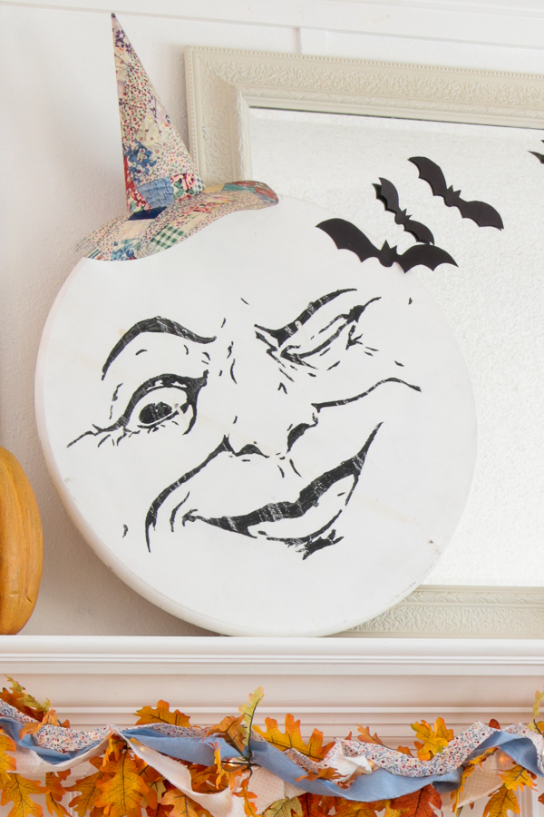 Man in the moon face wearing a quilted paper witch hat with black paper bats on the mirror