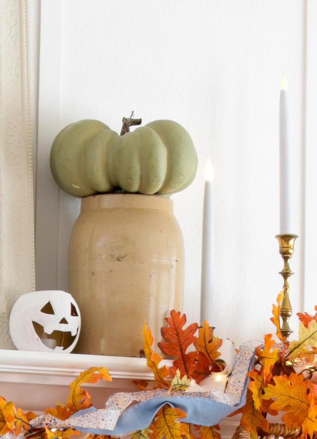 Sage green faux pumpkin in an old stoneware crock with a tiny white jack-o'-lantern and brass candlestick