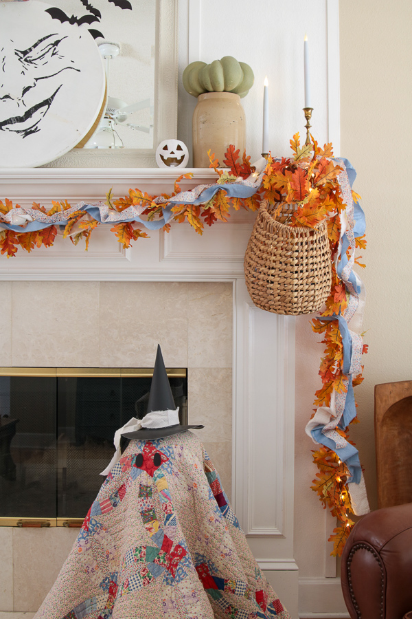 Whimsical cottage Halloween mantel with a moon face, green pumpkin in a stoneware crock, and leaf garland draping down the side