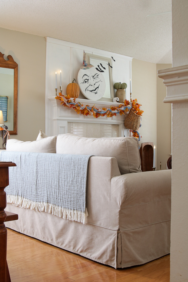 Chambray blue blanket draped over the back of a slipcovered sofa facing a Halloween mantel