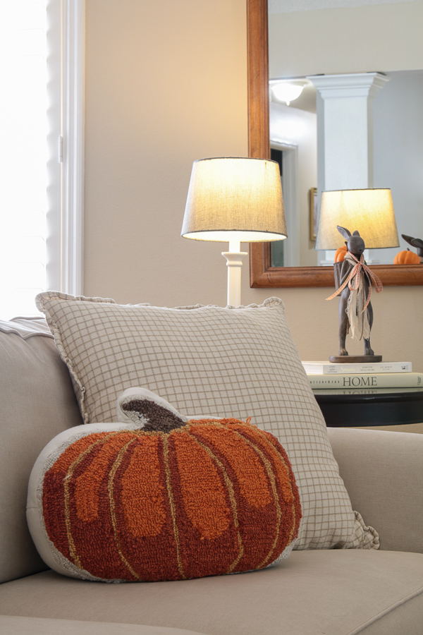 Hooked pumpkin pillow on a slipcovered sofa with a lamp and bunny statue in the background