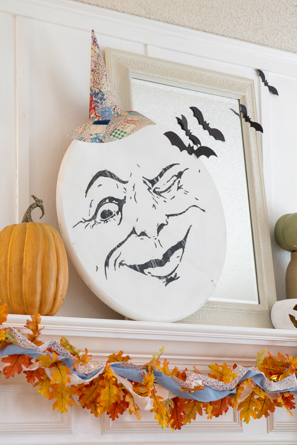 Black paper bat silhouettes flying across a mirror beside a moon face on a Halloween mantel