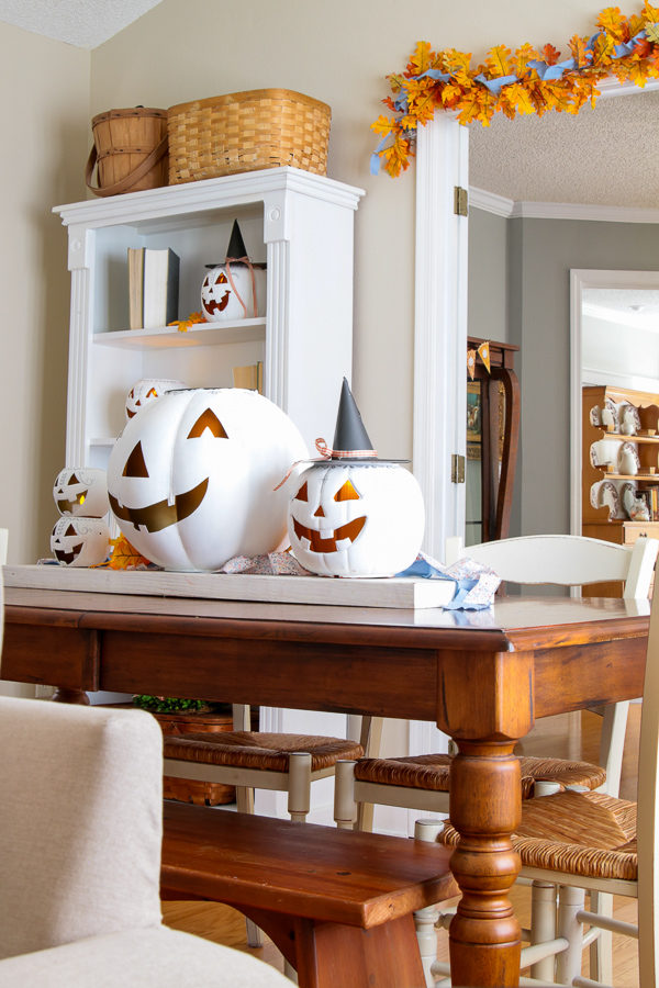 Dining table with a family of white painted jack-o'-lanterns on a rustic wood board in front of a bookcase